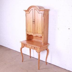 May include: A light wood desk with a hutch. The desk has three drawers and cabriole legs. The hutch has two doors and a shelf.
