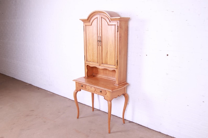May include: A light wood desk with a hutch. The desk has three drawers and cabriole legs. The hutch has two doors and a shelf.