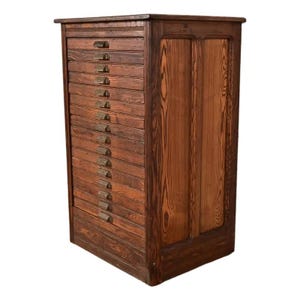 May include: A tall, antique wooden cabinet with numerous drawers. The cabinet is made of dark-stained wood, featuring visible wood grain and brass drawer pulls. The right side has a paneled design. A vintage storage solution.