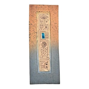 May include: A rectangular, textured wall hanging with a central panel featuring geometric designs and a blue square. The background transitions from a light orange to a gray-blue. The artwork has a vintage or antique aesthetic.