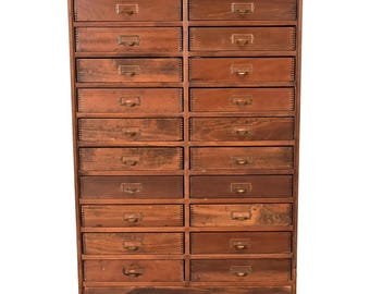 Op de afbeelding: Een vintage houten kast met twintig laden. De kast heeft een warme bruine kleur met messing lade grepen. De laden zijn gerangschikt in vijf rijen van vier laden elk. De kast is een klassiek meubelstuk.