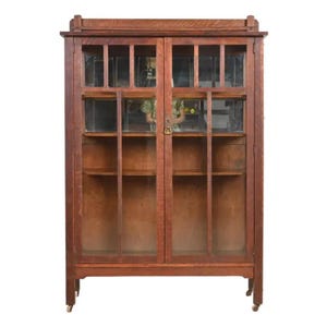 May include: A vintage wooden bookcase with glass doors and shelves. The bookcase has a dark brown finish and is on wheels.