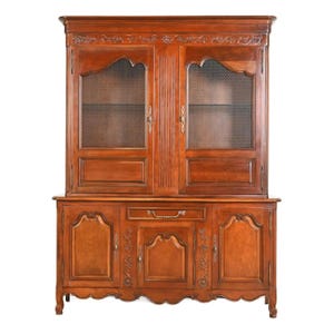 May include: A large, antique wooden cabinet with a warm brown finish. The upper section features two glass-fronted doors with wire mesh inserts. The lower section has three doors and a drawer, all adorned with ornate carvings and metal hardware.