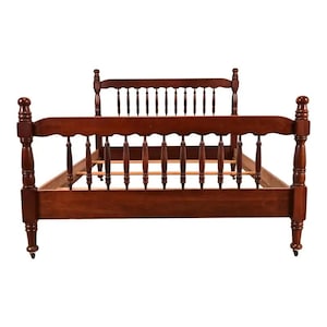 May include: A dark cherry-stained wooden bed frame with a headboard and footboard. The headboard and footboard have a spindle design. The bed frame has four rounded posts and is on small wheels.