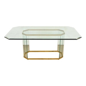 May include: A clear glass coffee table with an octagonal top and a gold-colored metal frame. The table has a geometric design and a modern aesthetic. The table is approximately 48 inches long and 36 inches wide.