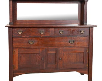 May include: A dark wood antique buffet with a mirrored back, three drawers, and two doors. The buffet has decorative brass hardware and sits on four legs.