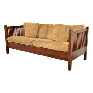 May include: A three-seat sofa featuring a dark brown wooden frame with vertical slat sides and back. The sofa includes two thick seat cushions and three back cushions upholstered in a textured, light tan fabric with a subtle pattern.