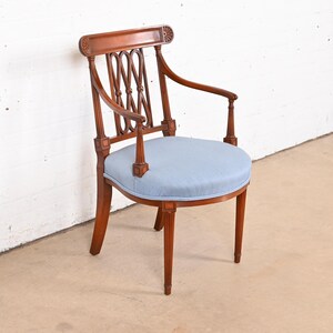 May include: A wooden armchair with a light blue upholstered seat and a carved back. The chair has a curved armrest and a fluted design on the legs.