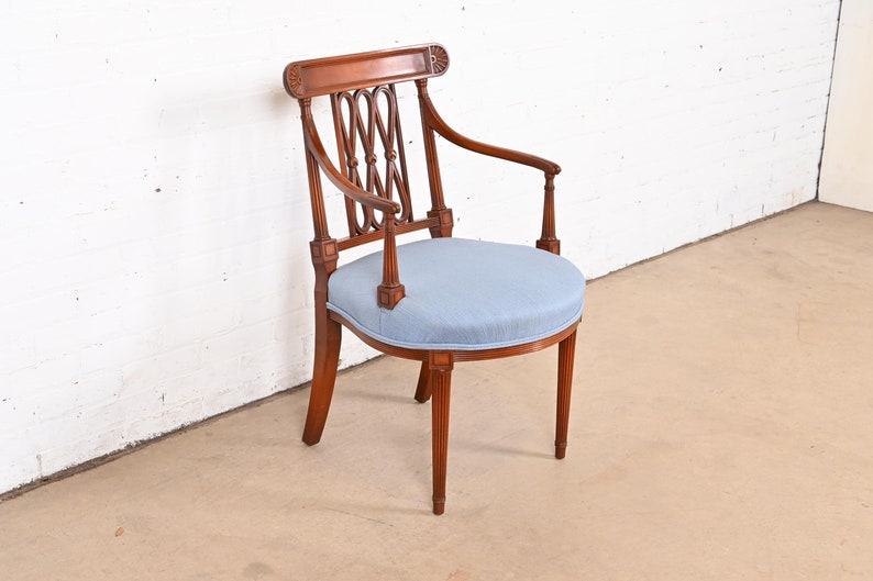 May include: A wooden armchair with a light blue upholstered seat and a carved back. The chair has a curved armrest and a fluted design on the legs.