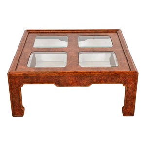 May include: Square coffee table with a reddish-brown finish and four glass inserts. The table has a decorative floral pattern around the edges and sturdy, curved legs. A stylish piece for a living room.