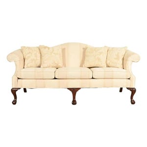 May include: A cream-colored three-cushion sofa featuring a subtle vertical stripe pattern, rolled arms, and four matching throw pillows. The piece is supported by dark brown wooden legs with a carved ball and claw foot design at the base.
