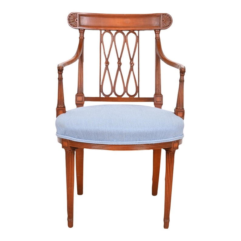 May include: A wooden armchair with a light blue fabric seat and a carved back. The chair has a rounded back and fluted legs.