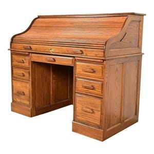 May include: A vintage wooden roll-top desk with multiple drawers and a pull-out writing surface. The desk is made of light brown wood and features a curved roll-top design. The desk has a keyhole and several drawers on both sides.
