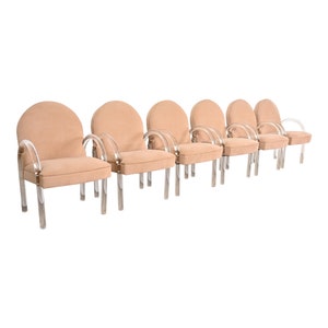 May include: Six beige upholstered chairs with clear acrylic frames and arms. The chairs are arranged in a row.