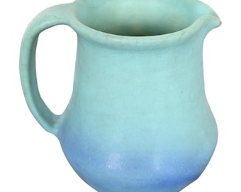 May include: A ceramic pitcher with a rounded body and a curved handle. The pitcher has a light blue to blue ombre effect. The spout is slightly pointed. The pitcher is likely used for serving beverages.
