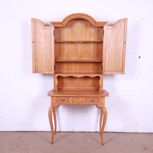 May include: A wooden hutch with a cabinet on top and a desk underneath. The cabinet has two doors that are open, revealing shelves inside. The desk has a drawer and a small shelf. The hutch is made of light wood and has a simple design.