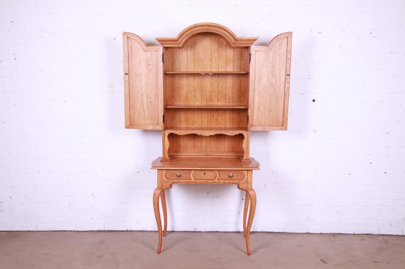 May include: A wooden hutch with a cabinet on top and a desk underneath. The cabinet has two doors that are open, revealing shelves inside. The desk has a drawer and a small shelf. The hutch is made of light wood and has a simple design.