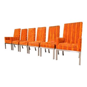 May include: Set of six vintage dining chairs. The chairs have a high back and armrests, upholstered in orange fabric with vertical stripes. The legs are made of silver metal. The chairs are arranged in a row.