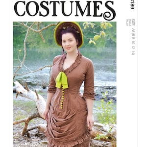 May include: McCall's Costumes pattern M8189. A woman models a brown dress with a green bow and buttons. The dress has a ruffled neckline and sleeves. She wears a matching hat with a green brim. The background is a natural outdoor setting.