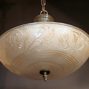 May include: A vintage pendant light with a frosted glass shade. The shade is bowl-shaped with an embossed floral pattern and a decorative metal finial. The light hangs from a chain.