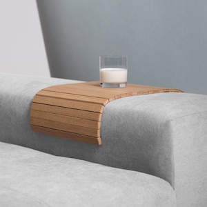 May include: A wooden tray with a curved design sits on a grey sofa. A glass of milk sits on the tray.
