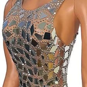 May include: A sleeveless floor-length dress featuring a sheer nude-colored base fabric adorned with an intricate mosaic of reflective silver mirror shards and small metallic studs arranged in a geometric pattern, including a high side slit.