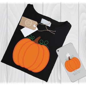 May include: Black t-shirt with a large orange pumpkin graphic and green vines. A matching pumpkin design is on a smartphone. The shirt has a tag attached. The items are on a light wood grain surface.