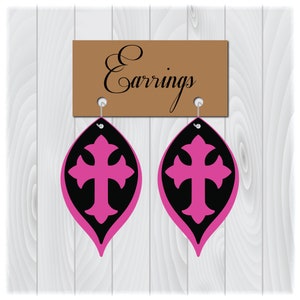May include: A pair of black and pink cross earrings. The earrings are shaped like a teardrop with a cross in the center. The earrings are hanging from a brown sign that says "Earrings".
