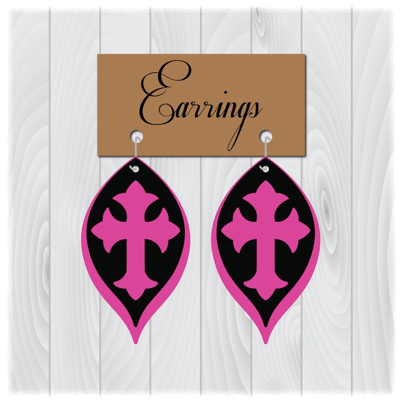May include: A pair of black and pink cross earrings. The earrings are shaped like a teardrop with a cross in the center. The earrings are hanging from a brown sign that says "Earrings".