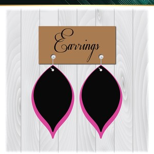 Pode incluir: Um par de brincos pretos e rosa com uma placa marrom que diz "Brincos". Os brincos t&ecirc;m a forma de uma l&aacute;grima com um contorno rosa. O fundo &eacute; um padr&atilde;o de madeira branca.