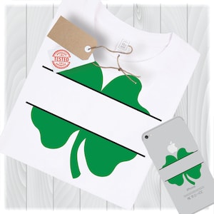 May include: A white t-shirt with a green four-leaf clover design. The clover is split in half with a black line, creating a space for text. The shirt is on a white wooden background.