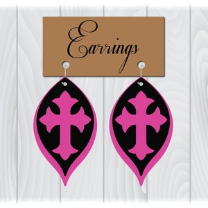 May include: A pair of pink and black earrings with a cross design. The earrings are hanging from a brown sign that says "Earrings".
