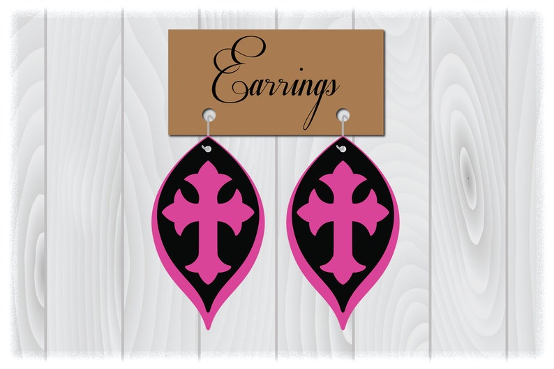 May include: A pair of pink and black earrings with a cross design. The earrings are hanging from a brown sign that says "Earrings".