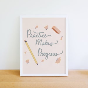 Op de afbeelding: Een ingelijst print met een roze achtergrond en de tekst "Practice Makes Progress" in grijs handschrift. De print bevat een geel potlood, een roze gum en potloodkrullen.