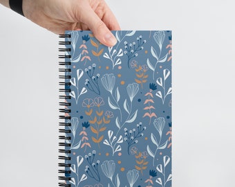 Peut inclure: Un carnet à spirales bleu avec un motif floral composé de fleurs et de feuilles blanches, roses et dorées.