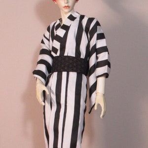 May include: A doll wearing a black and white striped kimono with a black obi belt. The doll has red hair and is wearing black boots.
