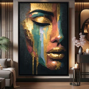 May include: A framed canvas art print featuring a close-up of a woman's face with closed eyes. The artwork uses a palette of gold, teal, orange, and pink, with gold accents on the lips and as dripping paint-like streaks.