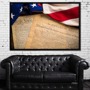 May include: Framed artwork featuring the American flag and historical documents. The flag displays red and white stripes with blue field and white stars. The documents include the text "We the People" and "In Congress, July 4, 1776".