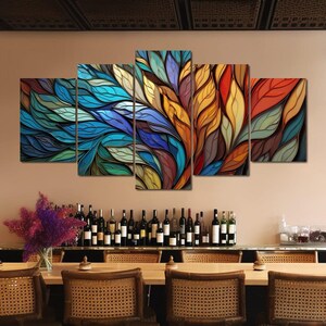 Op de afbeelding: Een vijfdelige abstracte canvas wandkunstset met een kleurrijk ontwerp van overlappende bladeren in tinten blauw, groen, geel, oranje en rood.