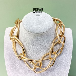 May include: A gold-toned chunky chain necklace with large, interlocking links. The necklace is displayed on a white mannequin bust.