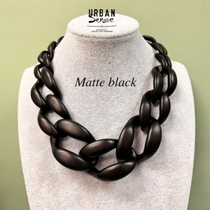 Könnte beinhalten: Matte schwarze, klobige Kettenkette aus Holz. Die Kette befindet sich auf einer weißen Mannequin-Büste. Der Text "Matte black" ist im Bild sichtbar.