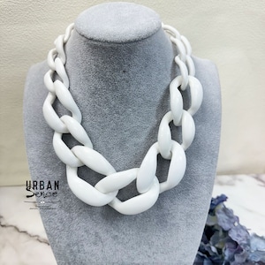May include: A white chunky chain necklace made of thick plastic links. The necklace is displayed on a gray mannequin bust.