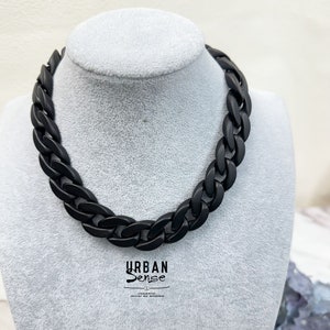 Puede incluir: Un collar de cadena negro con un diseño de eslabones gruesos y robustos. El collar se muestra en un maniquí.