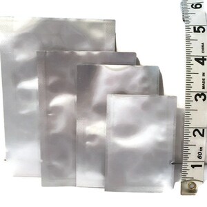 May include: Four clear plastic food storage bags of different sizes, measured against a tape measure. The bags are all clear and have a smooth, shiny finish. The tape measure is marked in inches and reads from 1 to 6.