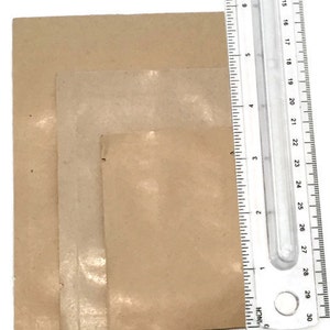 May include: Three brown paper bags of different sizes, measured with a ruler. The ruler is marked in inches and centimeters.