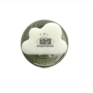May include: A small, white cloud-shaped soap rests on a United States quarter. The soap is smooth and wrapped in clear plastic. The soap has the text "SoapEmbeds" on it.
