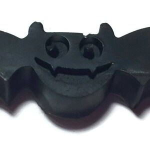 May include: A black bat-shaped decoration with a smiling face and pointed ears. The wings are spread wide, and the overall design is simple and cartoonish. This Halloween-themed item is likely a decorative accent.