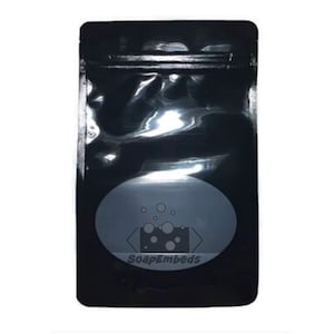 May include: Black stand-up pouch with a clear oval window. The window features a logo with the text "SoapEmbeds" and a graphic of a bar of soap with bubbles.
