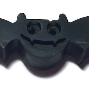 May include: A black bat-shaped rubber stamp with a carved out face, including eyes and a mouth.