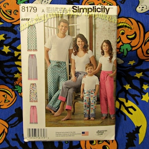 May include: Simplicity sewing pattern 8179 featuring pajama pants. The pattern includes various designs, including fish, checkered, and polka dot patterns. The package shows a family wearing the pajama pants. The text "easy-to-sew" is visible.